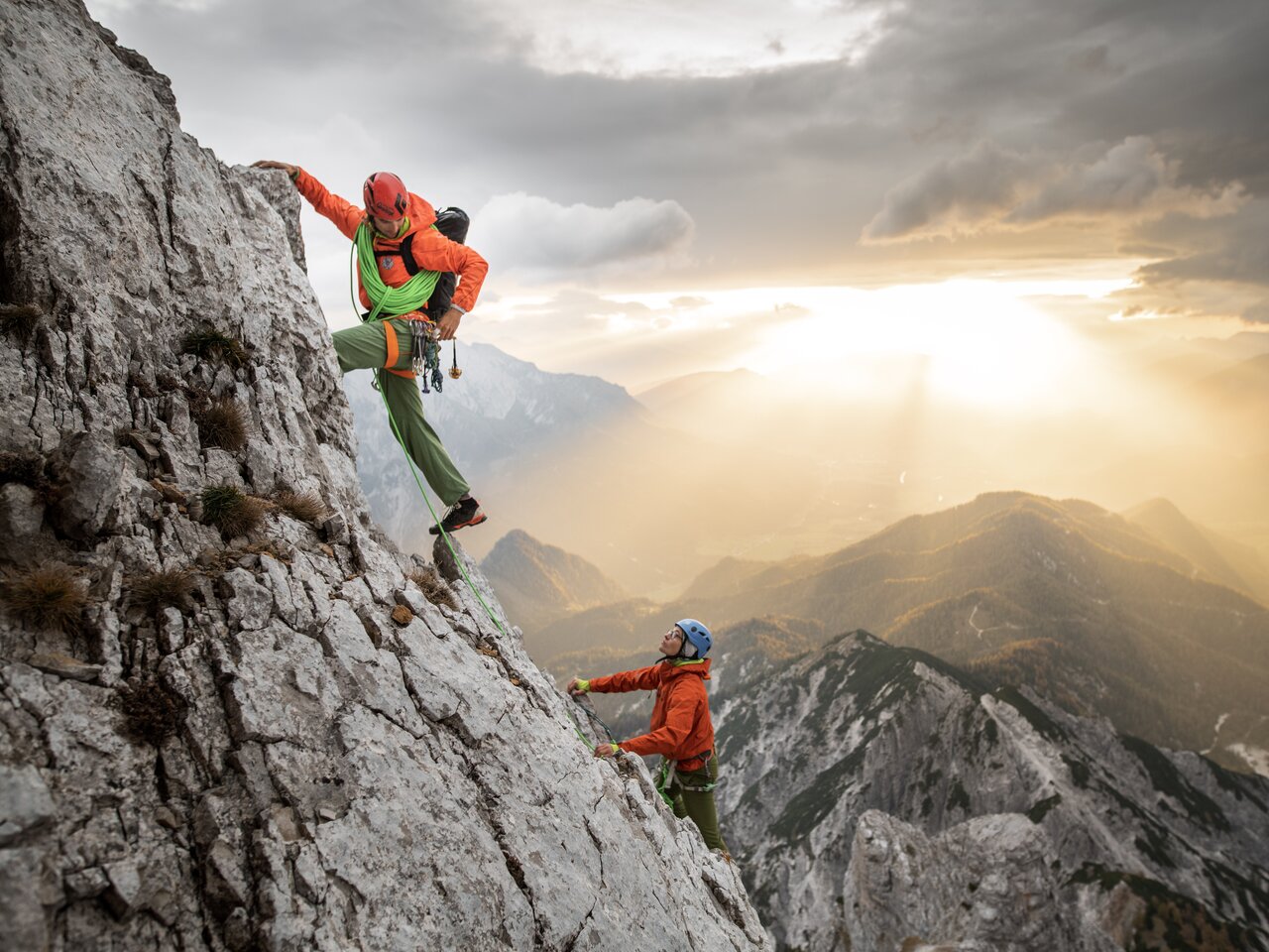Zwei Kletterer erklimmen einen steilen Felsen beim Sonnenuntergang.