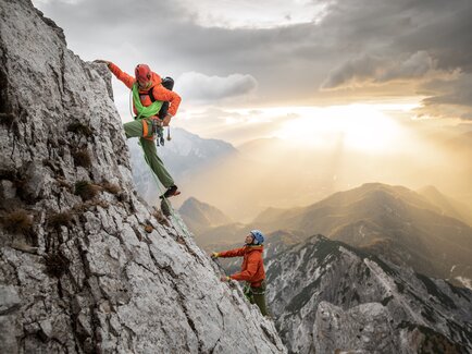 Zwei Kletterer erklimmen einen steilen Felsen beim Sonnenuntergang.