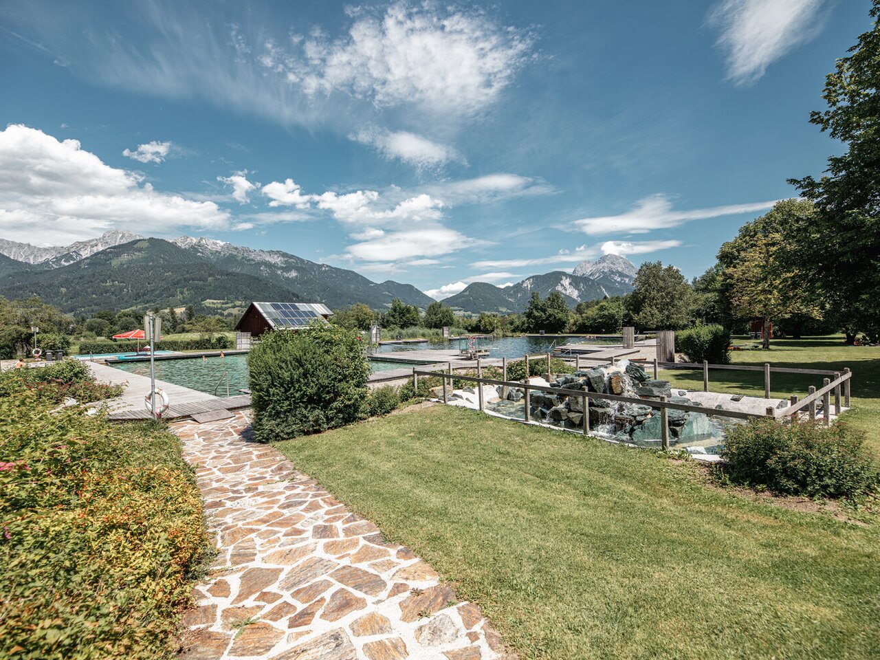 Beautiful garden with pool, surrounded by mountains and blue sky.