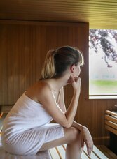 Frau sitzt in Sauna und genießt den Ausblick in die Natur