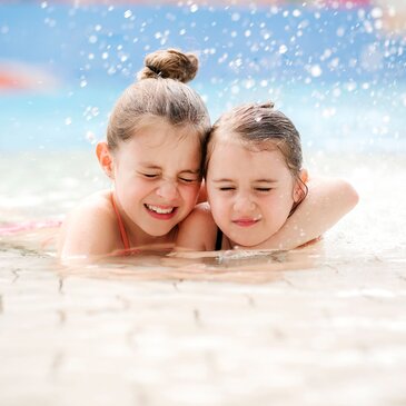Zwei Kinder spielen gemeinsam im Schwimmbad und genießen Wasserspaß im flachen Becken. Fröhliche Freizeit- und Familienaktivität im Wasser mit sommerlicher Atmosphäre.