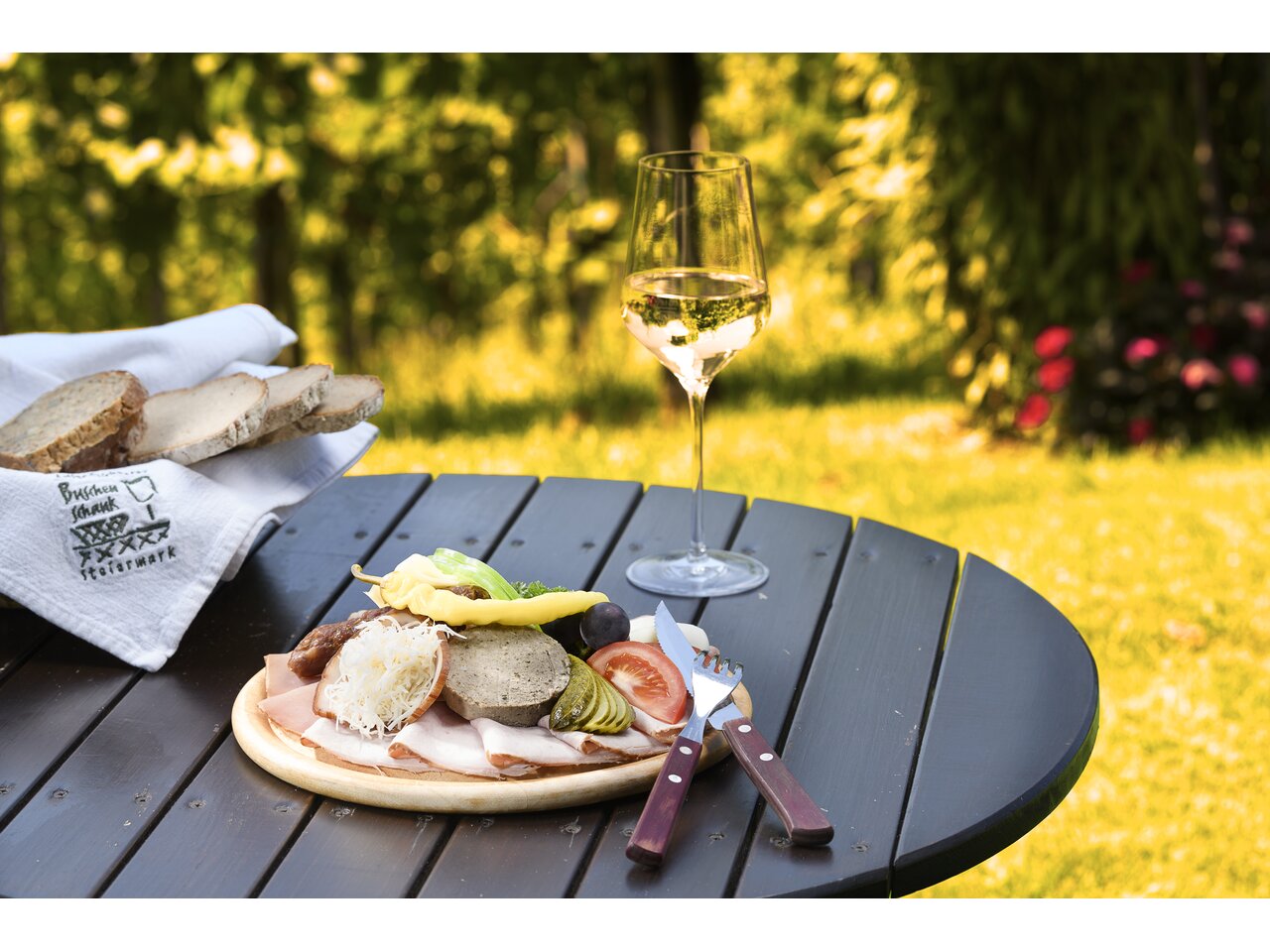 Steirische Brettljause mit einem Glas Wein am Gartentisch 