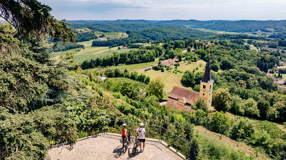 Radfahrer:innen beim Weingut Winkler-Hermaden mit Blick auf Kapfenstein und die Weinlandschaft im Thermen- & Vulkanland Steiermark.