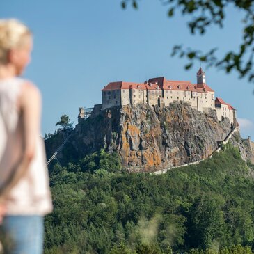 Eine Frau steht in der grünen, saftigen Wiese und genießt den Ausblick auf die imposante Riegersburg im Thermen- & Vulkanland Steiermark