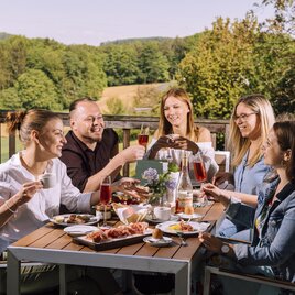 Gesellige Runde bei einer regionalen  Vulcano Schinken-Jause mit Schinken, Brot und Wein auf der Terrasse der Schinkenerlebniswelt   inmitten der grünen Hügellandschaft des Thermen- & Vulkanlands.