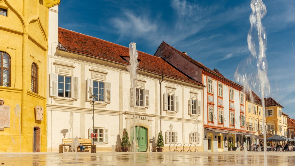 Historischer Hauptplatz in Bad Radkersburg mit barocken Fassaden und Wasserspielen, sonniger Tag mit blauem Himmel im Thermen- & Vulkanland, in der Südoststeiermark.