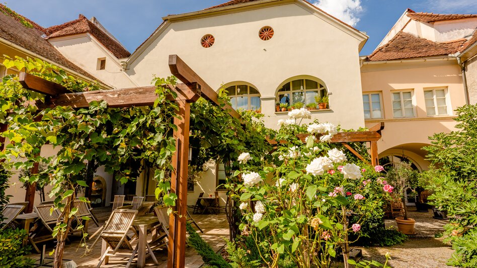 Idyllischer Schanigarten in Bad Radkersburg mit Weinlaube, blühenden Rosen und Sitzplätzen in einem historischen Innenhof in der Südoststeiermark.