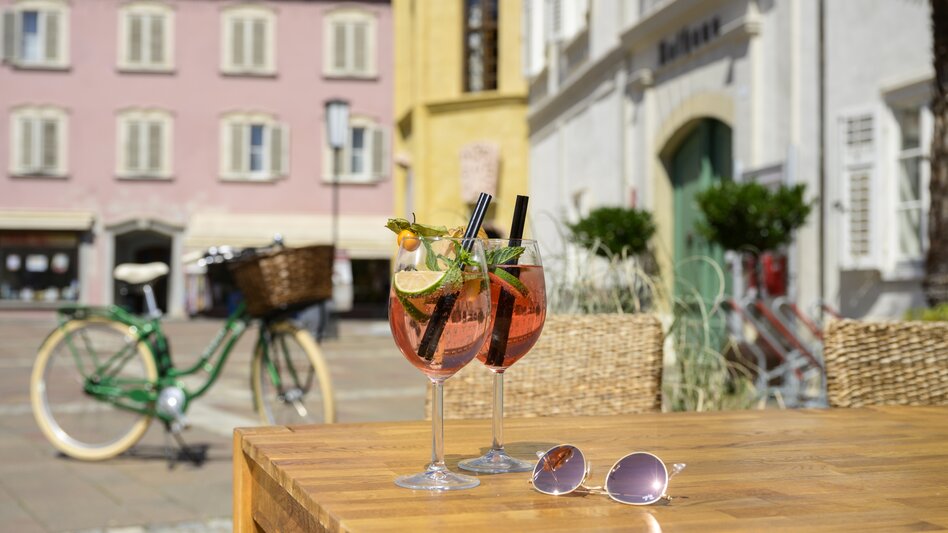 Aperitif in der Altstadt von Bad Radkersburg mit zwei Getränken auf einer sonnigen Terrasse und Fahrrad im Hintergrund – Genuss und Radurlaub in der Südoststeiermark.