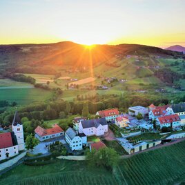 Sonnenuntergang über grünen Hügeln, steilen Weinhängen und der Kirche in St. Anna am Aigen im Thermen- & Vulkanland Steiermark