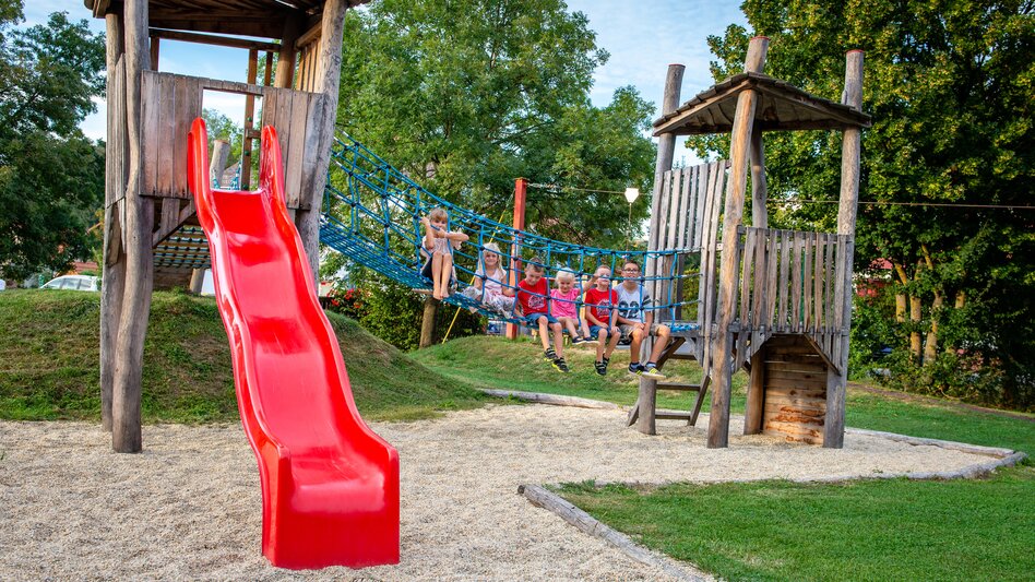 Kinder auf einem naturnahen Spielplatz mit Rutsche und Kletterelementen in Unterlamm im Thermen- & Vulkanland.