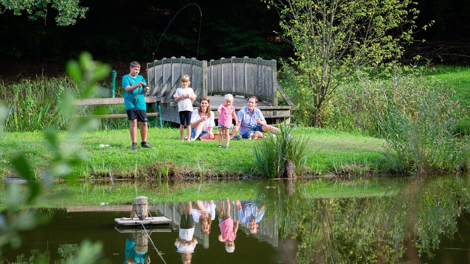 Familie mit Kindern bei einem Naturteich in Unterlamm, umgeben von Wiesen und viel Grün im Thermen- & Vulkanland.