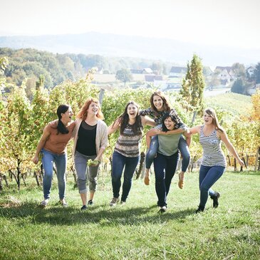 Sechs Winzer:innen hüpfen und lachen zwischen den Weinreben