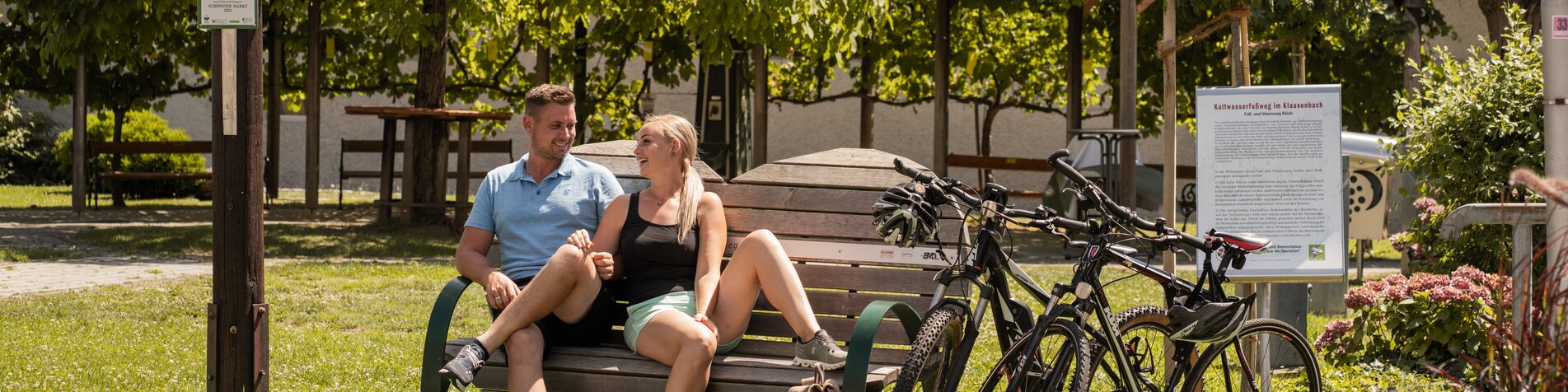 Rastplatz für Radfahrende im Ortsgebiet von Klöch in der Steiermark mit Sitzbank, zwei Fahrrädern und Wegweisern zu Gruisla, Klöchberg und Deutsch Haseldorf – typische Station für einen Radausflug durch die Weinregion.