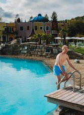 Junger blonder Mann steigt ins Thermalbecken im Rogner Bad Blumau