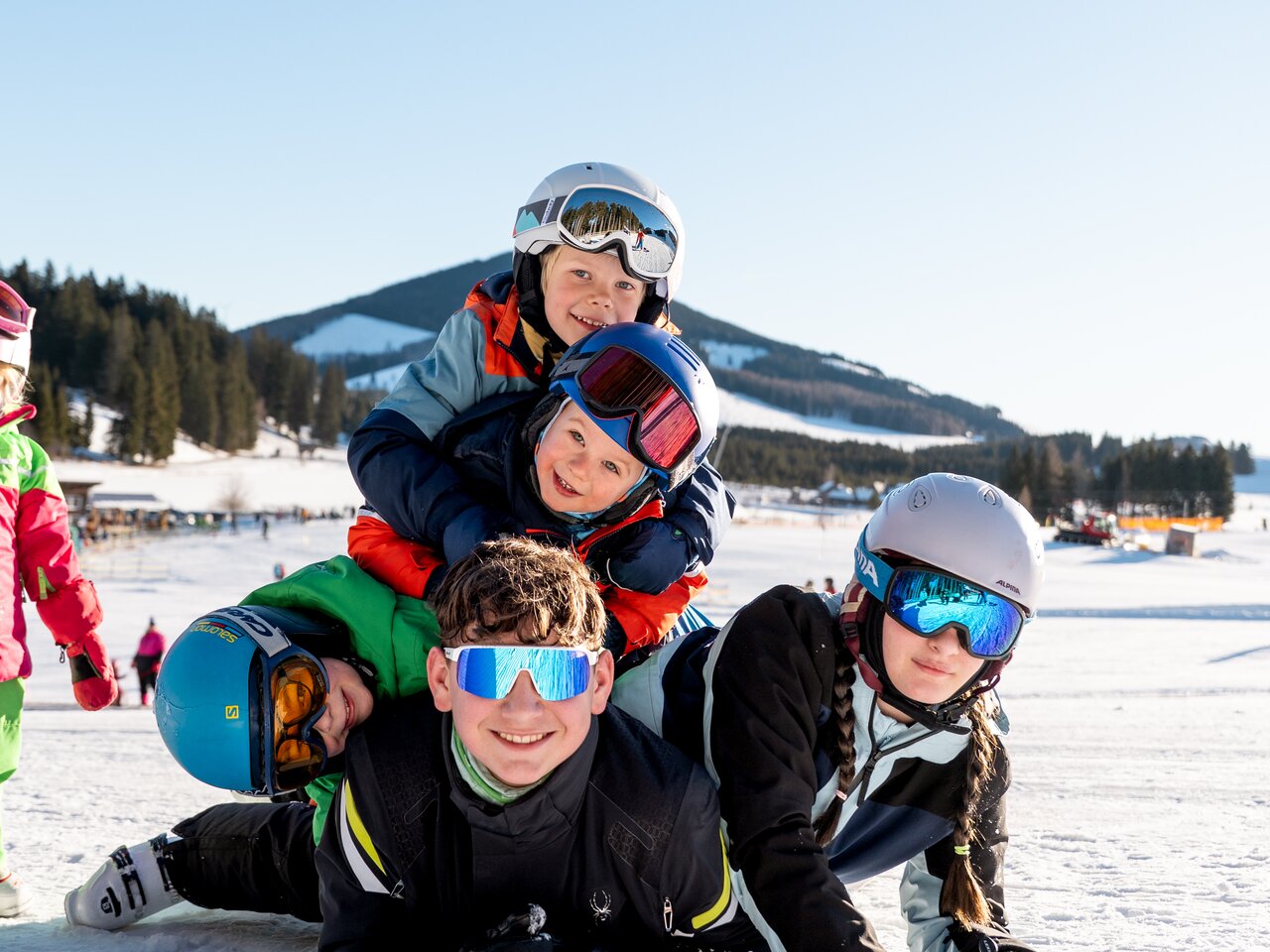 Vier Kinder posieren fröhlich im Schnee mit Skiausrüstung.