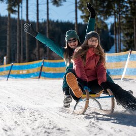 Zwei Frauen genießen das Rodeln im Schnee und strahlen vor Freude.
