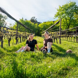 Zwei Frauen sitzen im Weinberg und genießen die Sonne.