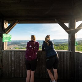 Zwei Wanderer genießen die Aussicht vom Türmchen auf die Landschaft.