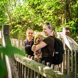 Zwei Frauen lächeln und halten einen Hund in der Natur.