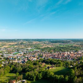 Weite Landschaft mit einem Dorf im Fokus, grüne Felder und blauer Himmel.