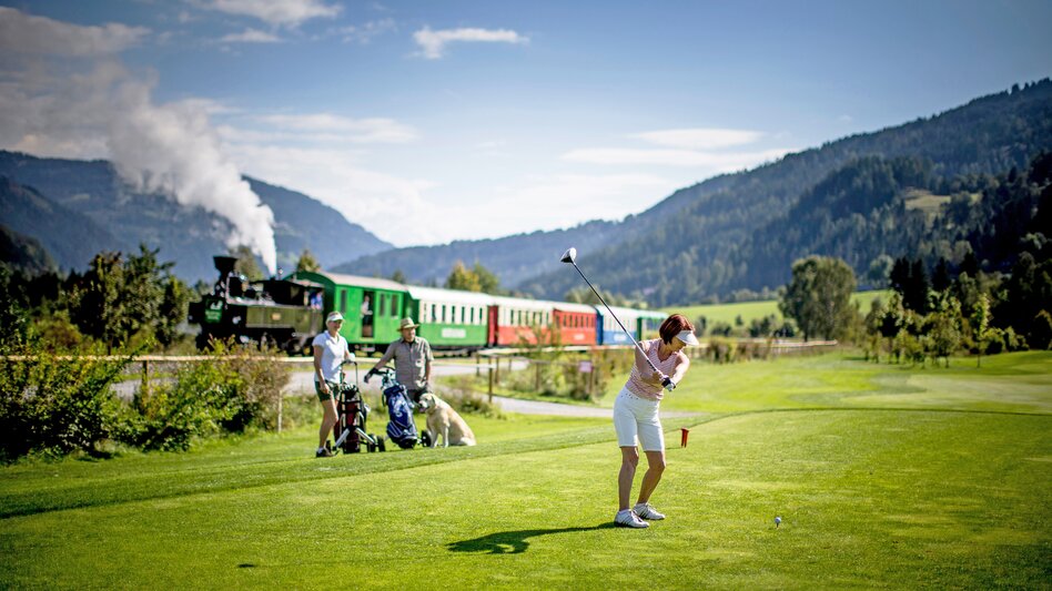 Golfspielen und im Hintergrund fährt die Murtalbahn