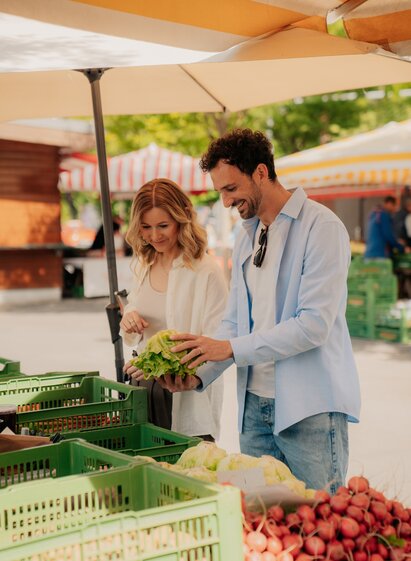 Two people selecting fresh vegetables at Kaiser Josef Market in Graz.