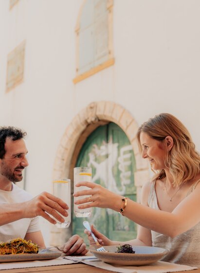 Two people toasting with drinks while dining outdoors in Graz.
