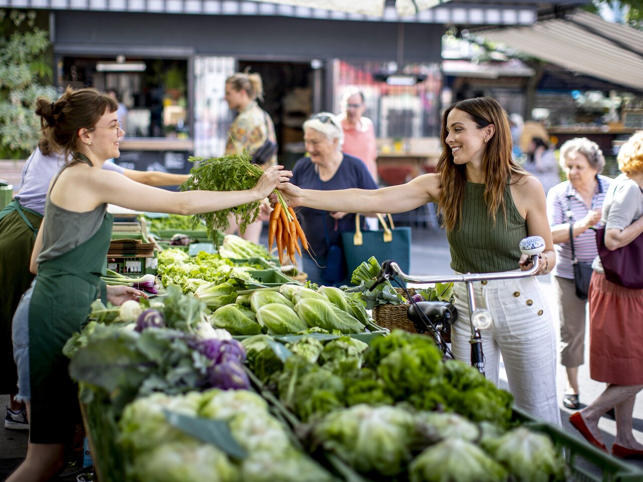 Market scene at Kaiser-Josef-Markt in Graz: Person purchasing fresh vegetables from a female vendor