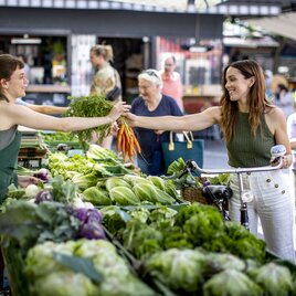 Marktszene am Kaiser-Josef-Markt in Graz: Eine Person kauft frisches Gemüse bei einer Bäuerin am Stand
