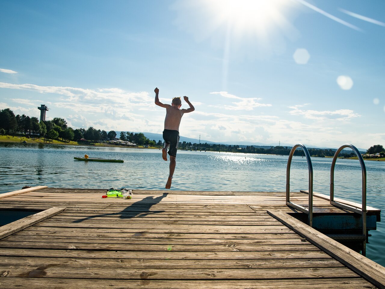 A child jumping off a wooden pier into Schwarzlsee, captured mid-jump in bright sunlight