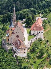 Luftaufnahme der Wallfahrtskirche Maria Straßengel, umgeben von grünen Hügeln und Wäldern.