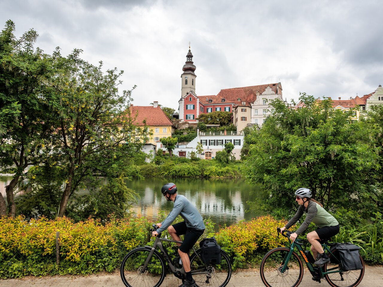Zwei Radfahrer radeln entlang des Murradwegs in Frohnleiten mit der Skyline im Hintergrund
