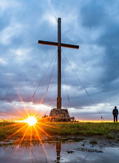 Sunrise at the summit of Schöckl with the summit cross, hikers and panoramic views over the Graz region.