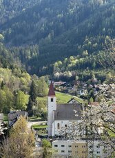 Blick auf Übelbach mit Kirche, blühenden Bäumen und bewaldeten Hängen in der Region Graz.