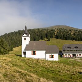 Gleinalm Schutzhaus mit der Kirche Maria Schnee vor dem Speikkogel in der alpinen Landschaft der Steiermark.