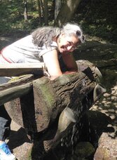 Wanderin nimmt ein Kneipp-Armbad an einer hölzernen Wasserstelle am Quellenweg in St. Radegund.
