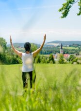 Person steht auf einer grünen Wiese an den Quellenwegen in St. Radegund mit Blick auf den Ort.