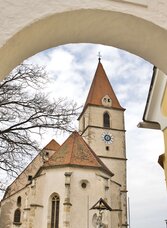 Blick durch einen Torbogen auf die Pfarrkirche Semriach mit Kirchturm und historischem Mauerwerk.