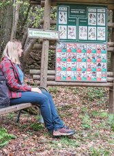 Wanderin rastet am Lehrwanderweg Semriach neben einer Infotafel zu heimischen Tieren und Pflanzen.