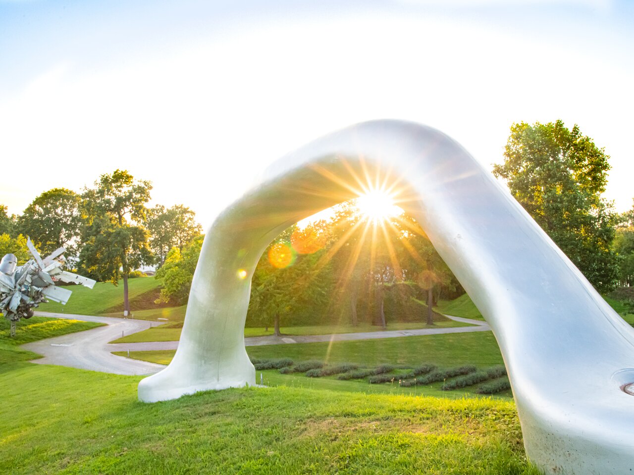 Abstract white sculpture in Sculpture Park Graz with sun rays in the background and green park landscape