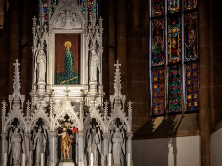 Detailaufnahme eines Kirchenaltars mit Statuen und Buntglasfenstern.
