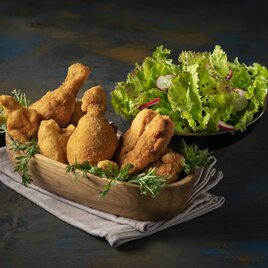 Knusprig gebackenes steirisches Backhendl in einer Holzschale, serviert mit frischem Krauthäuptel und Zitronenspalten