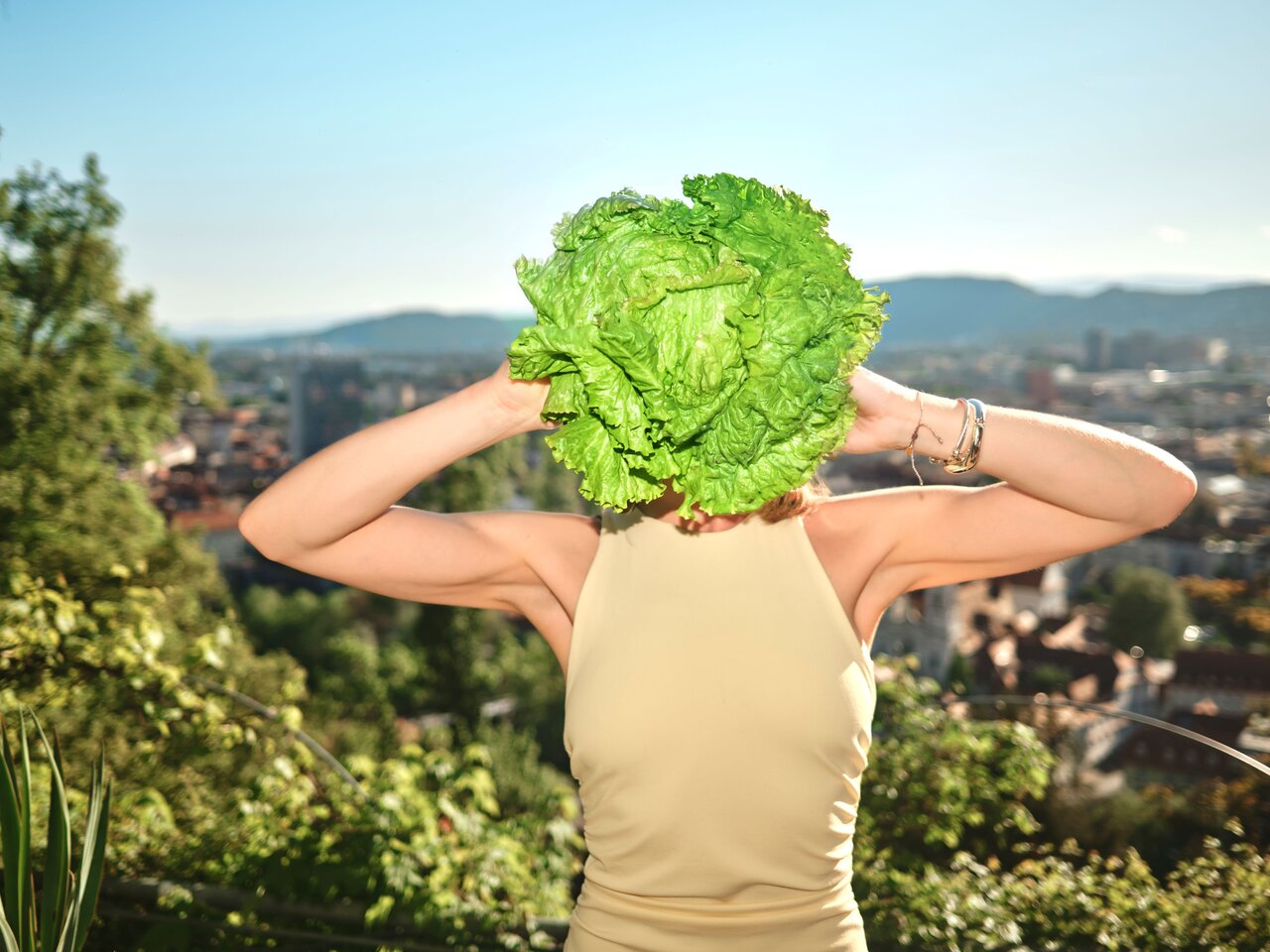 Person hält einen Grazer Krauthäuptel vor das Gesicht, mit Panoramablick über die Stadt Graz im Hintergrund.