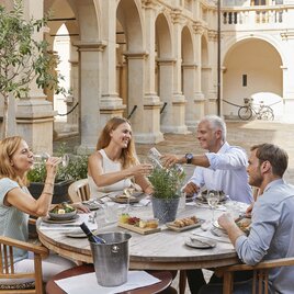 Vier Personen genießen ein Essen im historischen Landhaushof in Graz.  EN