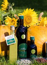 Products from Zachenegger Pumpkin Farm featuring Styrian pumpkin seed oil, pumpkin liqueur and pumpkin seeds displayed in front of freshly harvested pumpkins