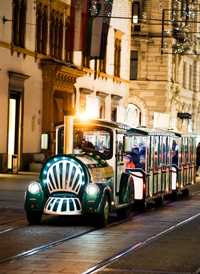 Eine festlich beleuchtete Bimmelbahn fährt am Abend durch die weihnachtlich geschmückte Altstadt von Graz. Menschen sitzen warm eingepackt im offenen Waggon.