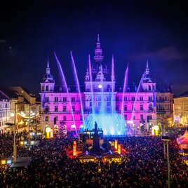 Silvesterspektakel am Grazer Hauptplatz mit beleuchteten Wasserfontänen und Publikum vor dem Rathaus.