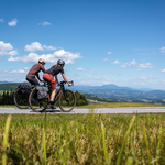 Zwei Radfahrer mit Helm auf Landstraße in der hügeligen Landschaft rund um Graz