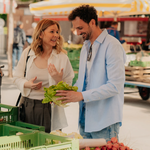 Paar kauft frisches Gemüse an einem Marktstand mit grünem Salat und Radieschen in Graz