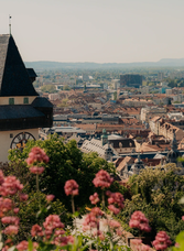 Graz Clock Tower on Schlossberg with view of the Old Town and blooming flowers in foreground
